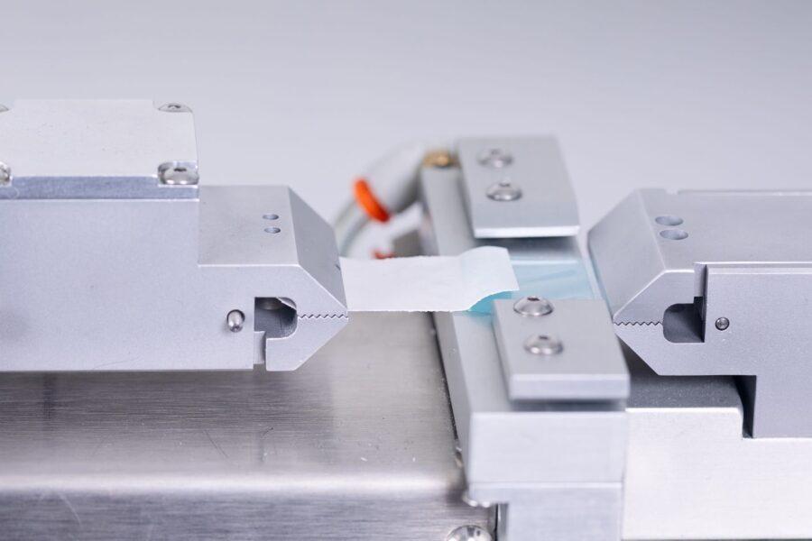 Laboratory peel test setup showing a medical device package being tested for seal strength